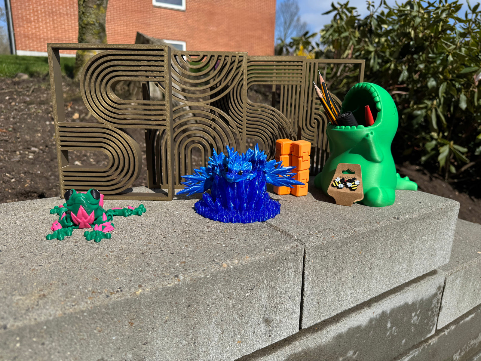 Billede af blandede 3d printede varer (4 små værker, frø med roser på, blå drage på en blå krystal, en uendelighed terning, et par øreringe og en blyantsholder)
