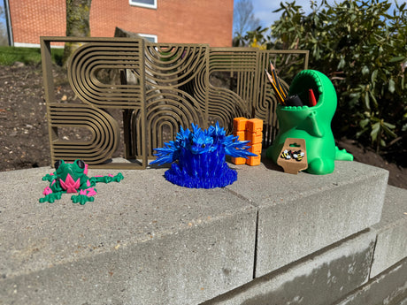 Billede af blandede 3d printede varer (4 små værker, frø med roser på, blå drage på en blå krystal, en uendelighed terning, et par øreringe og en blyantsholder)